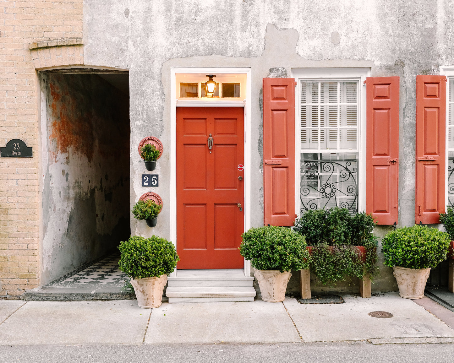 Bright red door with matching shutters and potted greenery at 25 Queen Street in Charleston – photo by Kelsey Bird