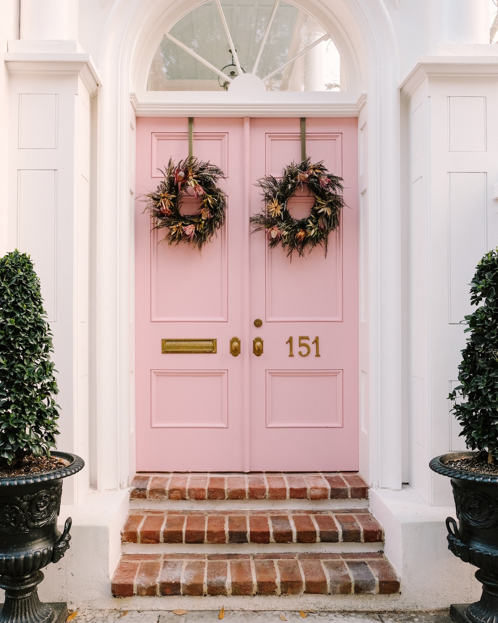 Pink double doors on a historic Charleston home with white trim and wreaths