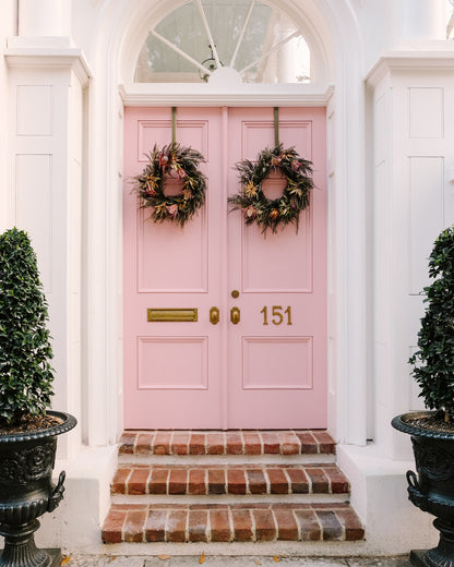 Pink double doors on a historic Charleston home with white trim and wreaths