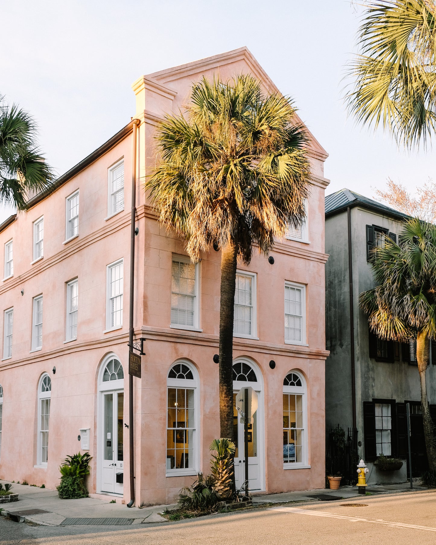 Tall palmetto trees beside a historic pink Charleston building under a blue sky